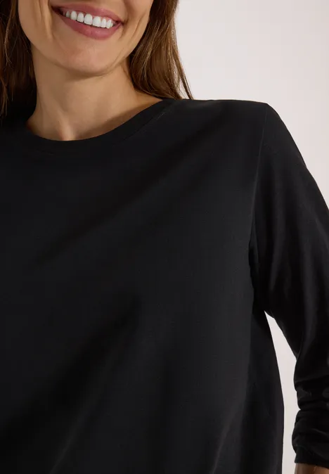 Eine Person trägt ein schwarzes Shirt mit Dreiviertelärmeln und rundem Ausschnitt, lächelt.