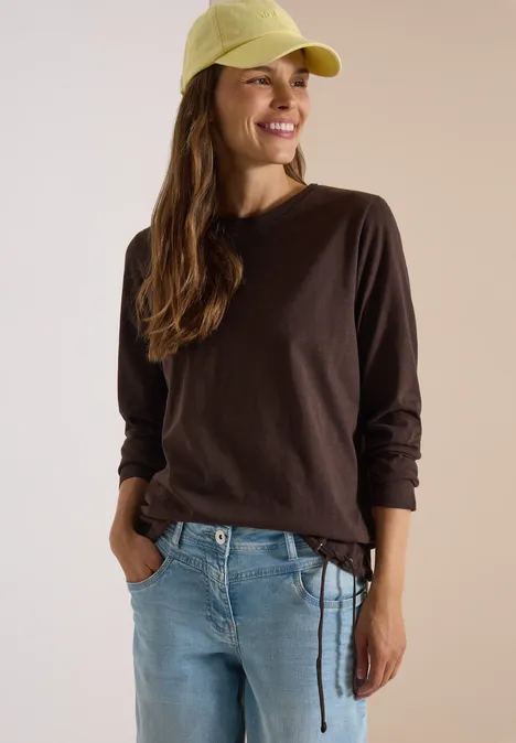 Langarm Shirt mit Rundhals und Tunnelzug truffle brown Junge Frau lächelt in braunem Langarmshirt, Jeans und gelber Schirmmütze vor hellem Hintergrund.