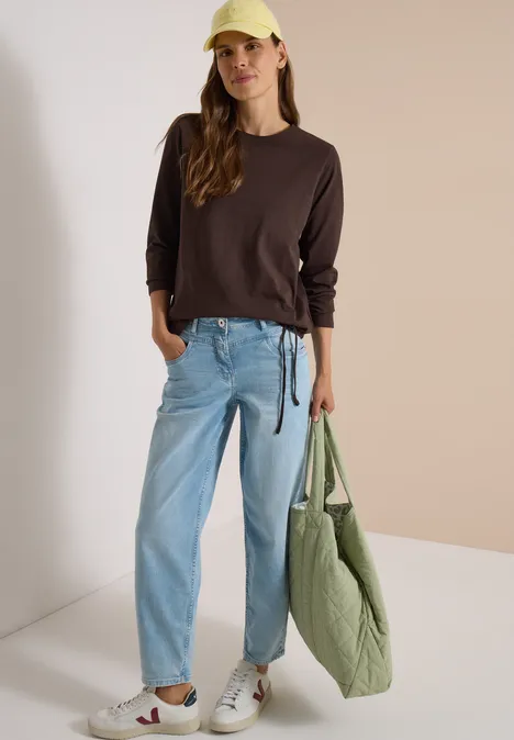 Langarm Shirt mit Rundhals und Tunnelzug truffle brown Eine junge Frau in lässigem Outfit: brauner Pullover, helle Jeans, weiße Sneaker, gelbe Mütze und große grüne Tasche.