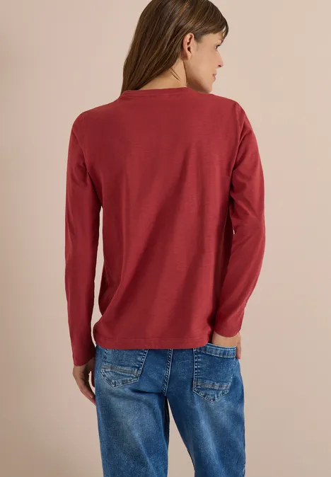 Langarm Shirt mit Rundhals und Tunnelzug russet red Frau steht mit dem Rücken zur Kamera, trägt rotes Langarmshirt und blaue Jeans.