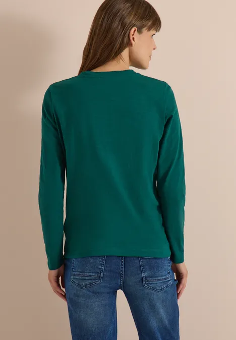 Langarm Shirt mit Rundhals und Tunnelzug dark fir green Frau von hinten trägt grünes Langarmshirt und blaue Jeans vor beigem Hintergrund
