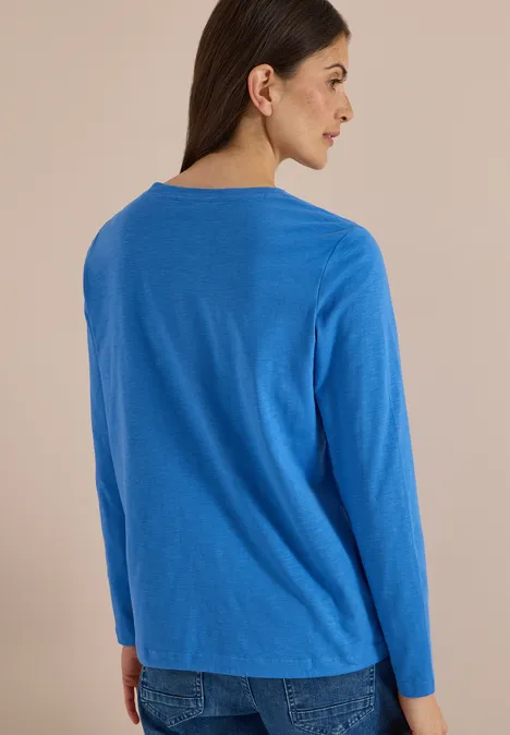 Vrouw van achteren in een blauwe trui met lange mouwen en een spijkerbroek voor een neutrale achtergrond.