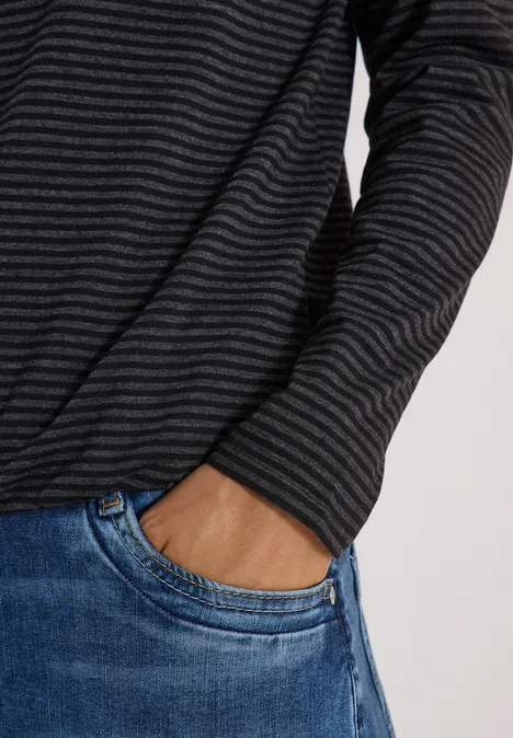 Person mit dunkelgrauem, fein gestreiftem Pullover, Hand in der Tasche einer blauen Jeans.