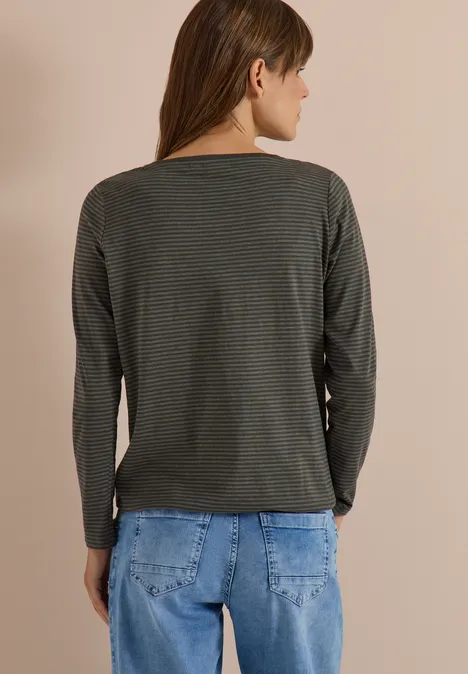 Eine Person steht mit dem Rücken zur Kamera und trägt ein dunkelgrünes, geringeltes Langarmshirt und blaue Jeans.
