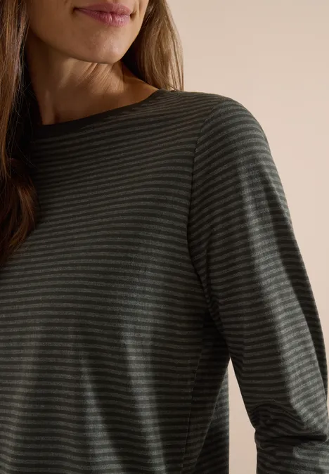 Nahaufnahme einer Person, die ein dunkelgrau-grün gestreiftes Langarmshirt vor hellem Hintergrund trägt.