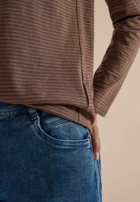 Langarm Shirt mit Boat Neck und Streifen urban taupe Person in braun gestreiftem Oberteil mit Hand in Jeans-Tasche vor beigem Hintergrund.