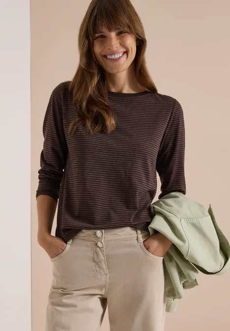 Langarm Shirt mit Boat Neck und Streifen truffle brown Lächelnde Frau in braunem Langarmshirt und hellen Hosen, hält eine grüne Jacke locker in der Hand.