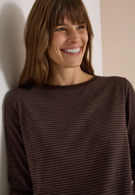 Langarm Shirt mit Boat Neck und Streifen truffle brown Eine lächelnde Frau mit braunen Haaren in einem gestreiften braunen Langarmshirt lehnt an einer weißen Wand.