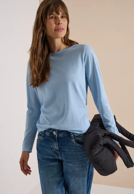 Eine Frau in hellblauem Langarmshirt hält eine schwarze Steppjacke.