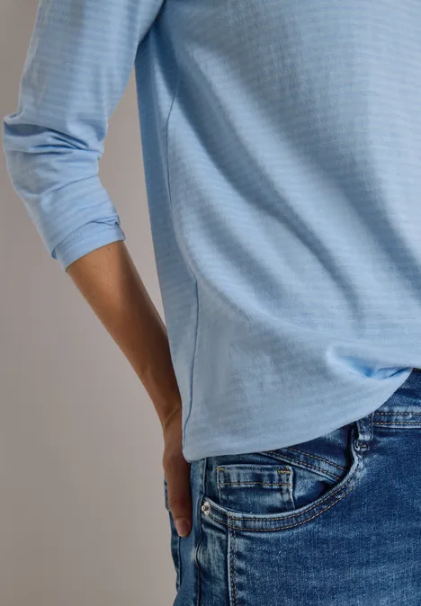 Seitliche Aufnahme einer Person in hellblauer 3/4-Arm-Bluse und blauer Jeans.