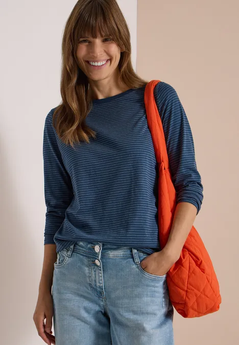 Langarm Shirt mit Boat Neck und Streifen moonlight blue Lächelnde Frau in blau gestreiftem Langarmshirt und Jeans, mit orangefarbener Stepp-Tasche über der Schulter.