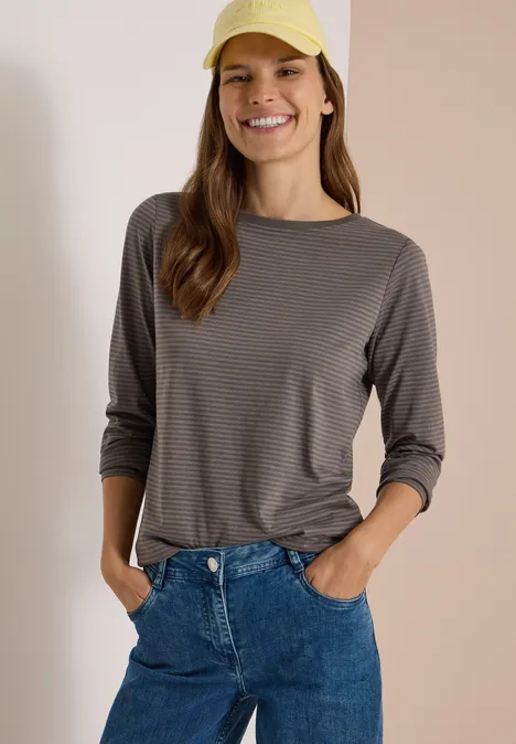 Langarm Shirt mit Boat Neck und Streifen storm grey Eine Frau lächelt, trägt gestreiftes Langarmshirt, blaue Jeans und gelbe Baseballkappe.
