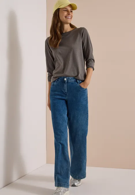 Langarm Shirt mit Boat Neck und Streifen storm grey Eine Frau trägt graues Langarmshirt, blaue Jeans, weiße Sneaker und gelbe Kappe und lächelt.