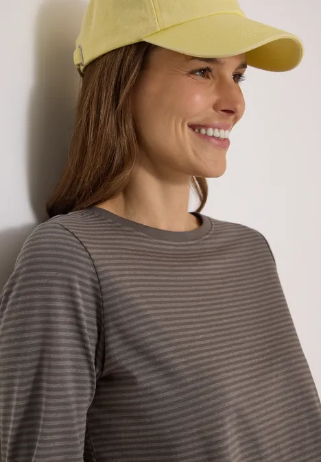 Langarm Shirt mit Boat Neck und Streifen storm grey Eine Frau mit gelber Kappe lächelt, trägt ein gestreiftes Shirt und lehnt an hellem Hintergrund.