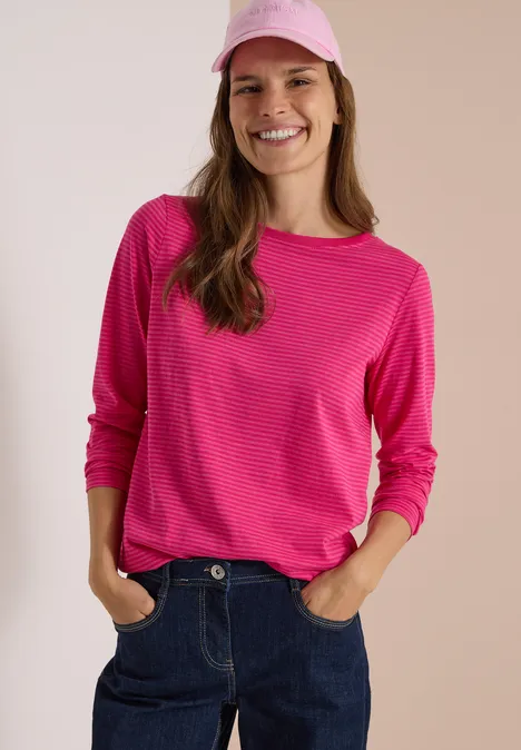 Langarm Shirt mit Boat Neck und Streifen pink flash Eine lächelnde Frau mit pinkem Shirt und Cap, lässig in Jeans posierend.