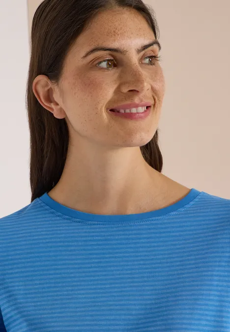 Portret van een jonge vrouw met donker haar en blauw gestreept shirt, glimlachend naar links.
