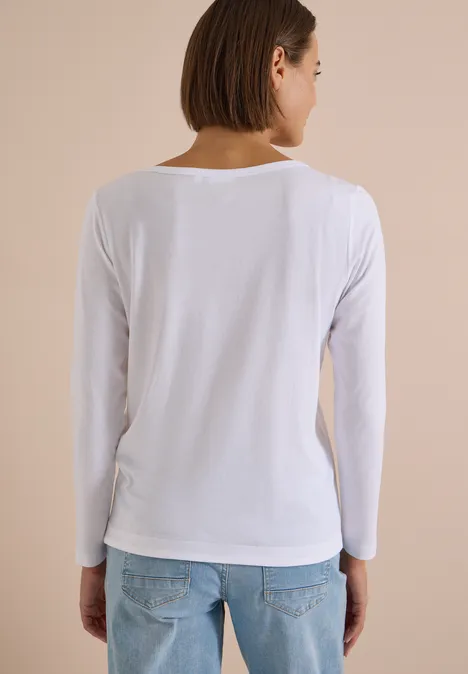Shirt mit Split Neck im Tunika-Look White Frau von hinten in weißem Langarmshirt und Jeans vor hellbeigem Hintergrund.