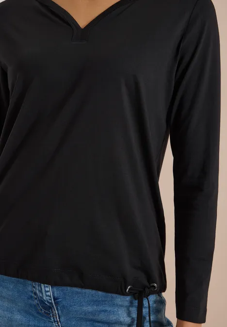 Shirt mit Split Neck im Tunika-Look Black Schwarzes V-Ausschnitt-Langarmshirt kombiniert mit blauen Jeans, Ansicht der Oberkörperpartie.