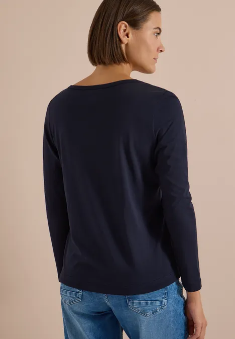 Shirt mit Split Neck im Tunika-Look urban dark blue Frau von hinten in dunkelblauem Langarmshirt und Jeans vor neutralem Hintergrund.