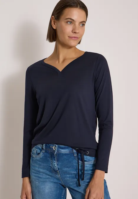Shirt mit Split Neck im Tunika-Look urban dark blue Frau in dunkelblauem V-Ausschnitt-Pullover und Jeans mit seitlichen Schnürungen, lässig posierend.