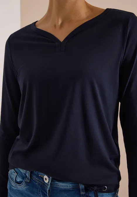 Shirt mit Split Neck im Tunika-Look urban dark blue Frau trägt ein dunkelblaues Langarmshirt mit V-Ausschnitt und Jeans vor hellem Hintergrund.