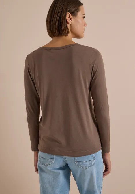 Shirt mit Split Neck im Tunika-Look urban taupe Frau von hinten in braunem Langarmshirt und blauen Jeans vor neutralem Hintergrund.