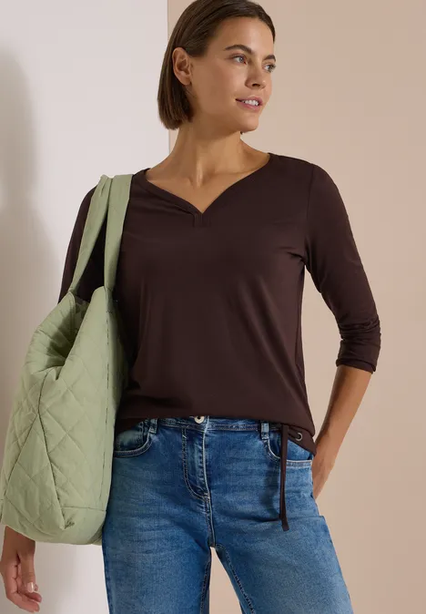 Shirt mit Split Neck im Tunika-Look truffle brown Frau mit dunklem V-Ausschnitt-Oberteil, blauen Jeans und gesteppten, hellgrünen Shopper über der Schulter.