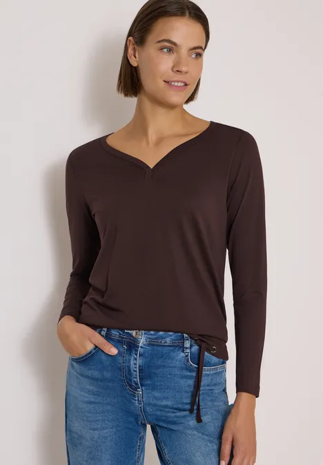 Shirt mit Split Neck im Tunika-Look truffle brown Frau trägt braunes Langarmshirt mit V-Ausschnitt und Jeans, eine Hand in der Tasche, lächelnd vor hellem Hintergrund.