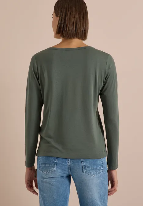 Shirt mit Split Neck im Tunika-Look dried olive green Person mit braunen Haaren von hinten, trägt grünes Langarmshirt und blaue Jeans vor beigem Hintergrund.