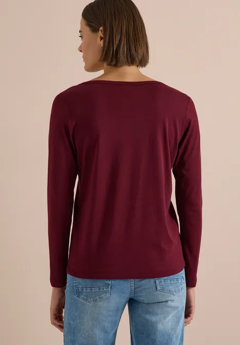 Shirt mit Split Neck im Tunika-Look red wine Frau von hinten mit langärmeligem bordeauxrotem Shirt und blauen Jeans vor neutralem Hintergrund.
