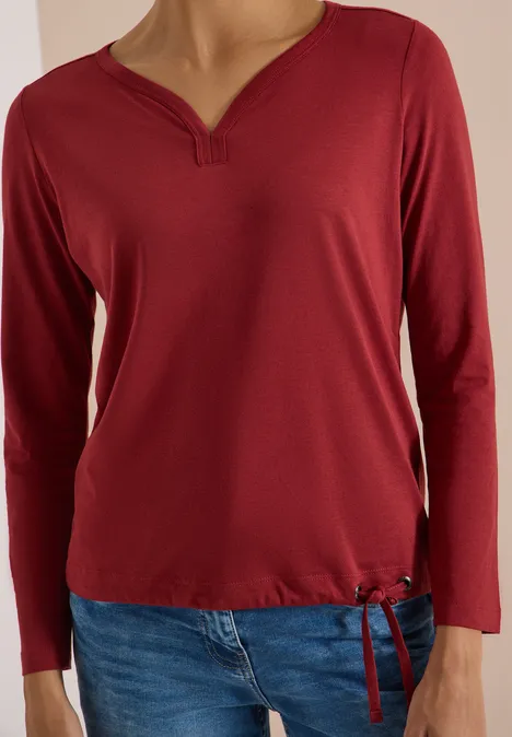 Shirt mit Split Neck im Tunika-Look russet red Rotes Langarmshirt mit V-Ausschnitt und Kordelzug am Saum, dazu blaue Jeans.