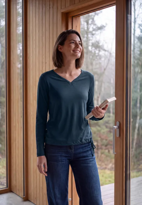 Shirt mit Split Neck im Tunika-Look moonlight blue Frau steht lächelnd an Glastür, hält Smartphone und blickt in einen bewaldeten Garten.