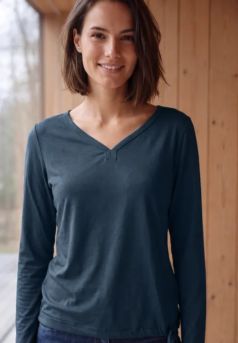 Shirt mit Split Neck im Tunika-Look moonlight blue Junge Frau in blauem V-Ausschnitt-Langarmshirt lächelt vor Holzverkleidung mit Fensterblick.