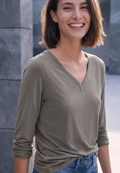 Shirt mit Split Neck im Tunika-Look storm grey Eine lächelnde Frau mit braunen Haaren trägt ein graues V-Neck-Langarmshirt und blaue Jeans.