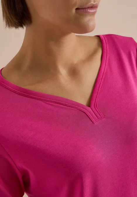 Nahaufnahme einer Person im pinken V-Ausschnitt-Shirt, Gesicht und Oberkörper nur teilweise sichtbar