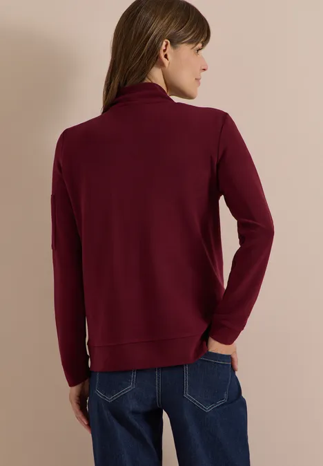Ottoman Blouson in Unifarbe red wine Rückenansicht einer Person in burgunderrotem Rollkragenpullover und Jeans vor beigem Hintergrund.