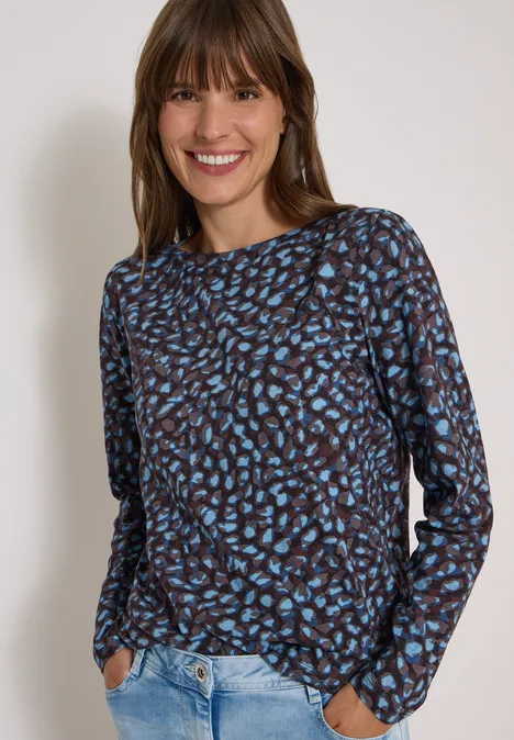 T-shirt à col bateau et motif patchwork raw chocolate brown Une femme souriante en chemise marron à motifs bleus et jean clair.