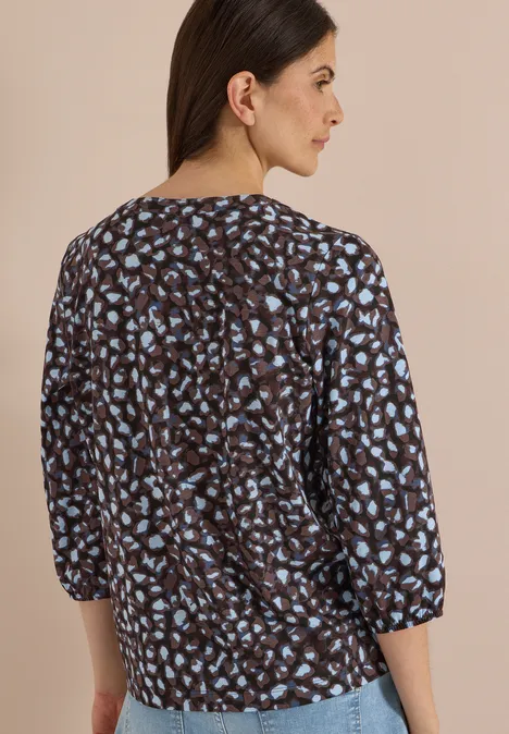 Frau von hinten in dunkelblauer Bluse mit hellblauem Fleckenmuster, 3/4-Ärmel, legere Passform.
