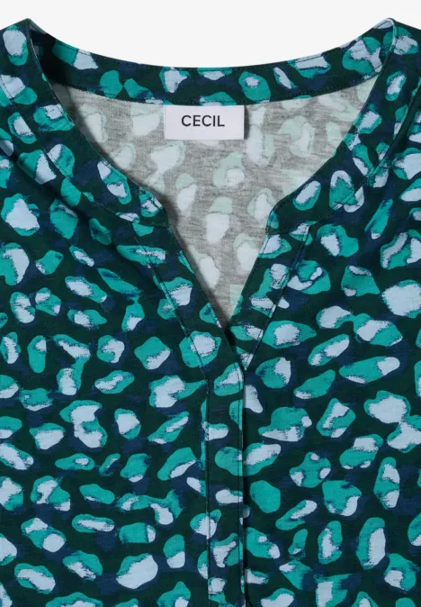 Grüne Bluse mit abstraktem Muster aus hellblauen und türkisen Flecken und V-Ausschnitt.