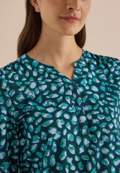 Nahaufnahme einer Frau in grünem Shirt mit blau-weißen Herzmustern und kleinem V-Ausschnitt.
