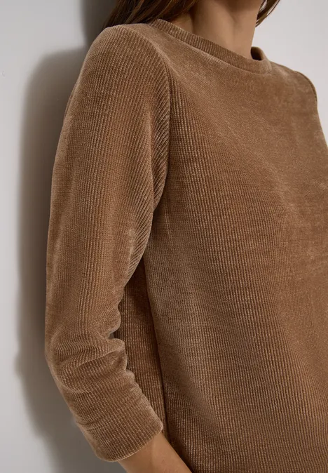 T-shirt à manches 3/4 en velours côtelé avec encolure bateau creamy mocha Buste vêtu d’un pull en velours côtelé marron, adossé de manière décontractée à un mur blanc.