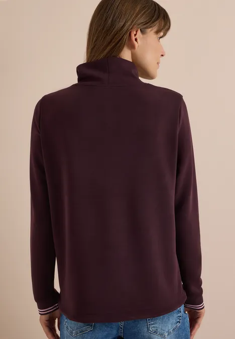Rückenansicht einer Person in dunkellila Rollkragenpullover und blauer Jeans.