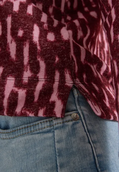 Nahaufnahme der seitlichen Hüfte in blauen Jeans und rotgemustertem Oberteil mit seitlichem Schlitz.