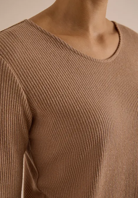 Nahaufnahme einer Person im beigen, gerippten Pullover-Oberteil.