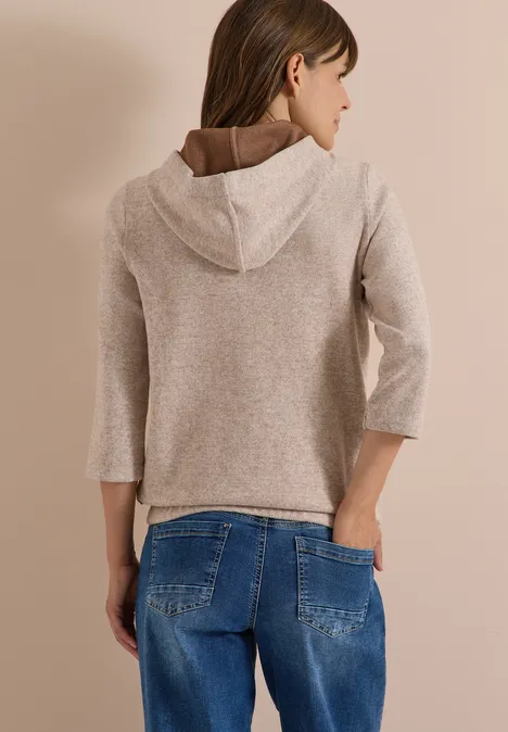 Vue de dos d’une femme portant un pull à capuche beige et un jean bleu