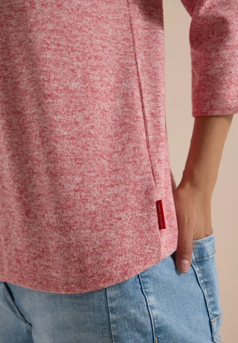 Haut rose chiné à manches 3/4 avec fente latérale et petite étiquette rouge, porté avec un jean.