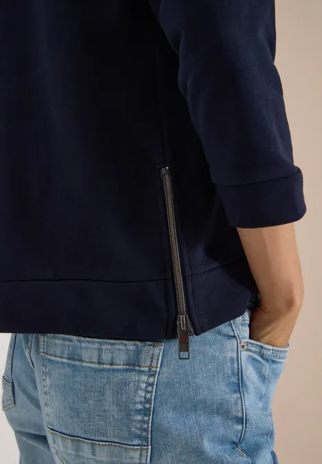 T-shirt à manches 3/4, col rond et inscription urban dark blue Personne en sweat bleu marine avec fermeture latérale et jean bleu, main dans la poche.