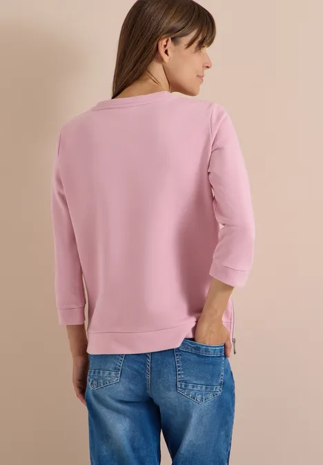 T-shirt à manches 3/4, col rond et inscription mellow rose Femme de dos portant un haut rose à manches 3/4 et un jean, devant un fond clair.