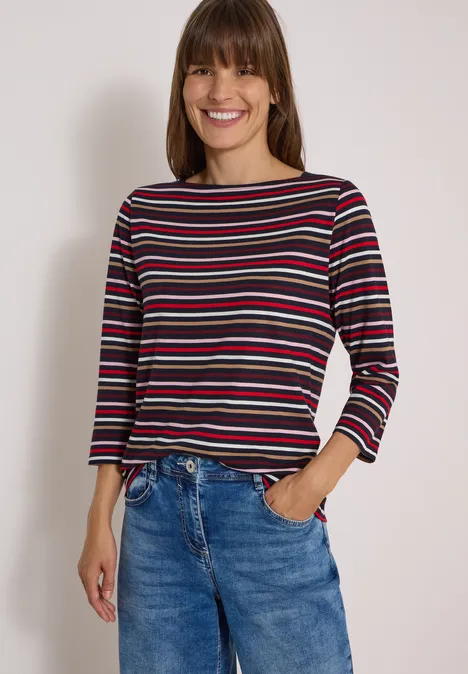 Frau in gestreiftem Langarmshirt und blauen Jeans lächelt in die Kamera.