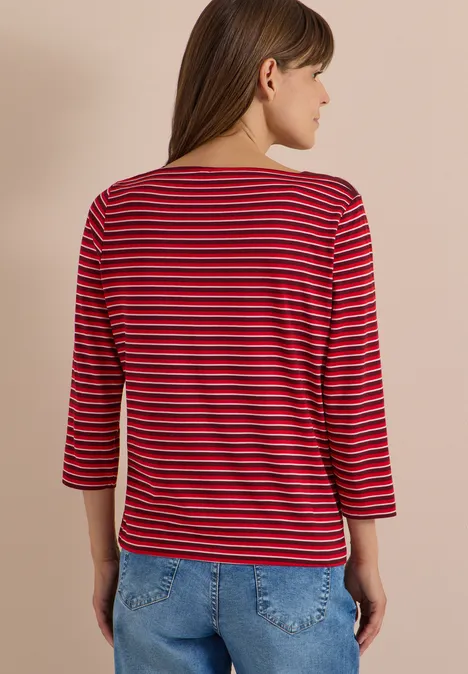 Frau von hinten in rot-schwarz gestreiftem 3/4-Arm-Shirt und Jeans vor hellem Hintergrund.